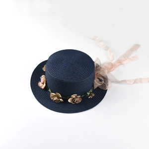 Detail of navy straw hat featuring intricate weave and beige floral wreath with chiffon ribbon