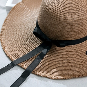 Détail d'un chapeau de paille d'été avec bords effilochés et élégant ruban noir