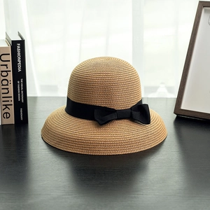 Detailed texture of light brown cloche straw hat with black ribbon bow on wooden surface