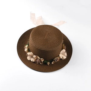 Close-up of flat top straw boater hat with floral trim and pink ribbon on white background