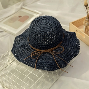 Detail of navy blue hand-woven straw hat with a brown bow on a white grid background