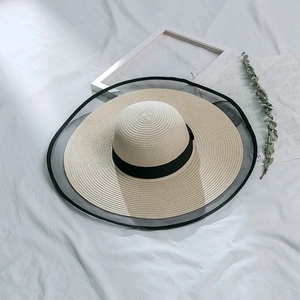Detail of wide brim straw hat with black mesh trim and decorative ribbon on fabric