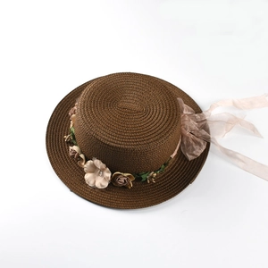 Close-up of brown flat-top straw hat with beige silk flowers and sheer organza ribbon