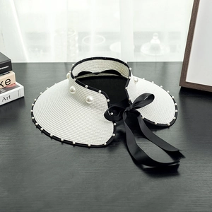 Detailed view of white straw sun visor featuring elegant pearls and a large black bow