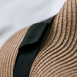 Macro shot of fine straw weave texture and black grosgrain ribbon detail on sun hat