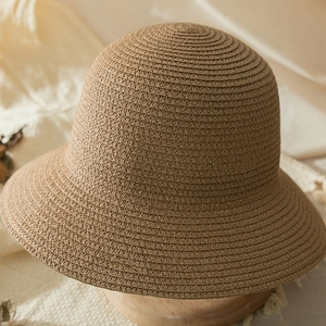 Detailed view of dark khaki woven straw sun hat with dense spiral texture on wooden stand