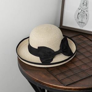 Dettaglio di un cappello di paglia con grande fiocco nero su piano in legno