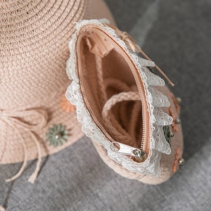 Macro detail of pink straw bag with white lace trim, daisy accents and metal zipper