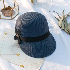 Détail d'un chapeau de paille bleu marine avec ruban noir élégant sur tissu blanc