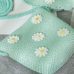 Close-up of mint green woven straw bag with delicate white daisy embroidery detail