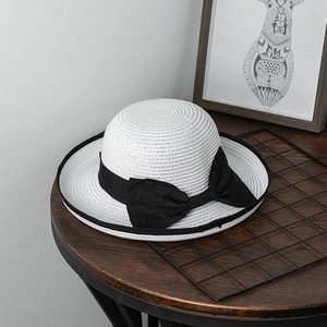 Dettaglio di un cappello di paglia bianco con fiocco nero su un tavolo di legno