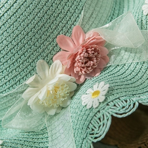Detailed view of mint green straw hat featuring handmade pink and white mesh flowers