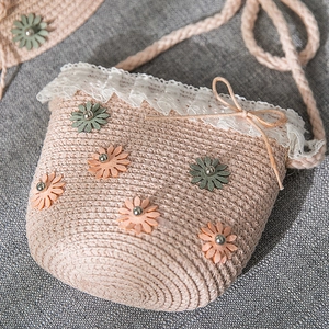 Close-up of pink straw crossbody bag with white lace, floral daisy decor, and bow detail