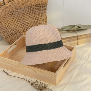Detail of handwoven pink straw hat with green ribbon texture on a wooden tray