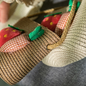 Détail d'un sac en paille tressée avec fraises et carottes en peluche pour filles
