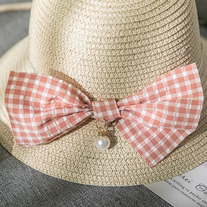 Detail of a straw hat with a pink checkered bow and a pearl pendant accessory