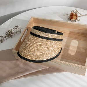 Detailed weave of natural straw sun visor hat with black fabric trim on wooden tray