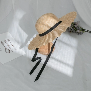 Detail of wide brim straw sun hat with wavy edges and elegant long black ribbons