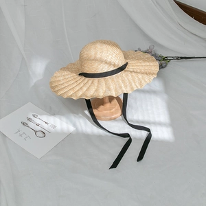 Detail of a wavy brim straw sun hat with black ribbons on a minimalist white linen background