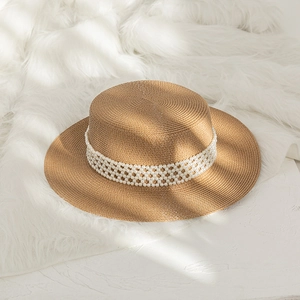 Detail of flat top straw hat with decorative pearl mesh band on beige woven material