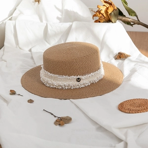 Detail of straw boater hat with white lace ribbon and M metal charm on woven texture