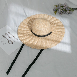 Detail of a wavy brim straw sun hat with black ribbons on white linen background