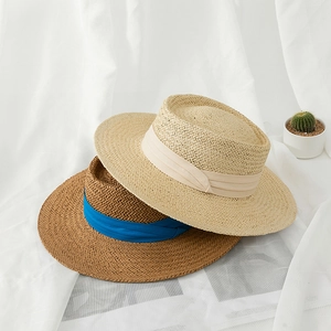 Detail of hand-woven straw boater hats with elegant ribbons on minimalist white fabric