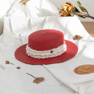 Detail of red boater straw hat featuring cream lace trim and metal M logo accent