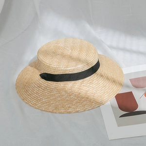 Détail d'un chapeau de paille à bord plat avec ruban noir sur un tissu blanc
