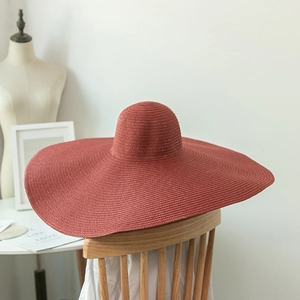 Detail of a large brim brick red straw hat with fine weave texture on a wooden chair