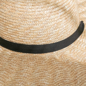 Close-up of the intricate weave and black ribbon detail on a wavy sun straw hat