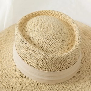 Close-up of a woven flat top boater hat with a pleated khaki ribbon for summer