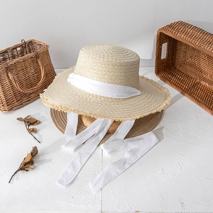 Close-up of beige straw sun hat featuring a delicate frayed brim and white fabric ribbon