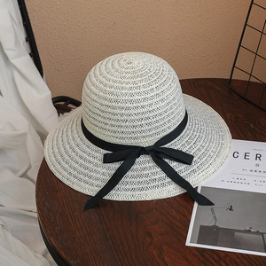Détail du chapeau de soleil beige en paille tressée avec ruban noir sur table en bois