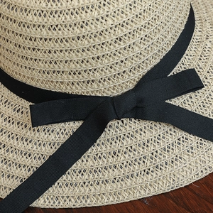 Détail d'un chapeau de paille beige avec un large ruban noir noué et un tissage précis