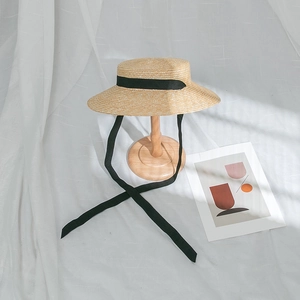 Détail d'un chapeau de paille à sommet plat avec tressage dense et rubans de soie noirs