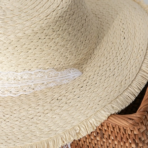 Detail of beige straw hat with delicate white lace ribbon and frayed raw edge texture