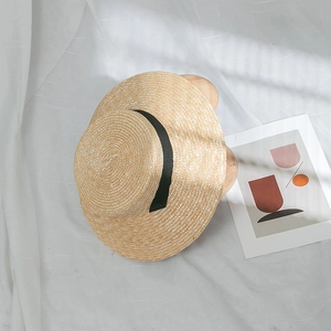 Vue à plat d'un chapeau de paille avec ruban noir sur fond de tissu blanc élégant