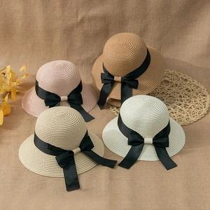 Handwoven straw cloche hats with black bow ribbons in multiple colors on rustic burlap