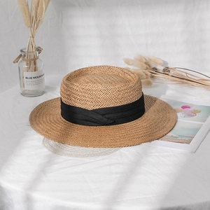 Close-up of natural woven boater hat with black ribbon detail on a textured white background