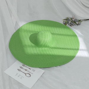 Wide brim bright green straw sun hat for women on white fabric with summer afternoon shadows
