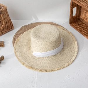 Close-up of summer straw sun hat with frayed brim and elegant white cotton ribbon band