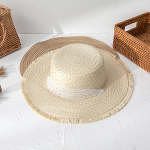 Top view of flat top straw hat with white lace ribbon and frayed edges on textured ground