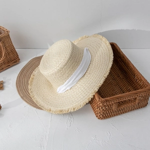 Straw sun hat with flat top, frayed edges and white ribbon bow for beach vacation