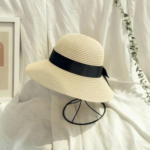 Elegant beige straw sun hat with a wide black ribbon bow on a modern wire hat stand