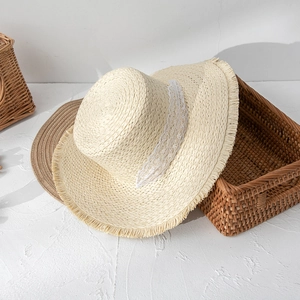 Detail of flat top straw hat featuring a white lace ribbon and frayed edge brim