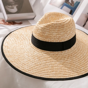 Close-up of wide brim straw hat featuring detailed woven texture and black ribbon trim
