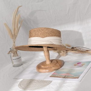 Close-up of straw boater hat with cream ribbon displayed on a wooden stand