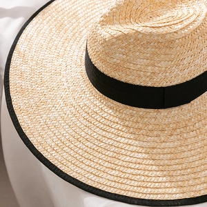 Close-up of a tightly woven straw sun hat with black grosgrain ribbon and piped edge