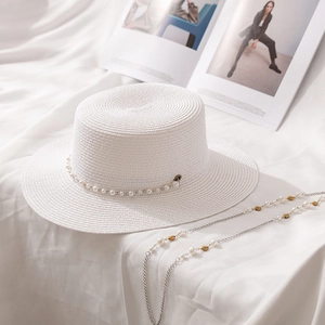 Détail d'un chapeau de paille blanc à bord plat avec perles et chaîne dorée